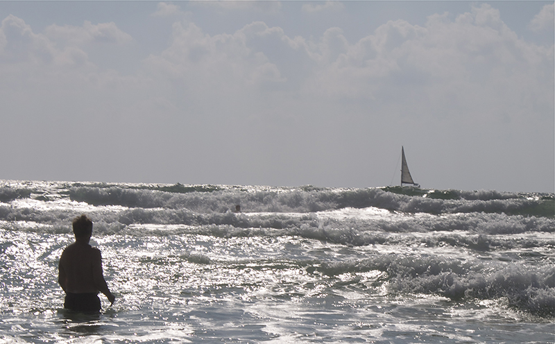 Gary wades into the surf as the “nes” of this sailboat fills with wind from an unseen source, propelling it forward off Israel’s coast
